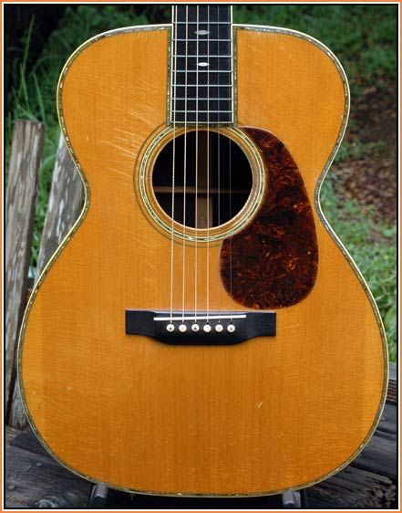 an old acoustic guitar sitting on top of a wooden table in front of a fence