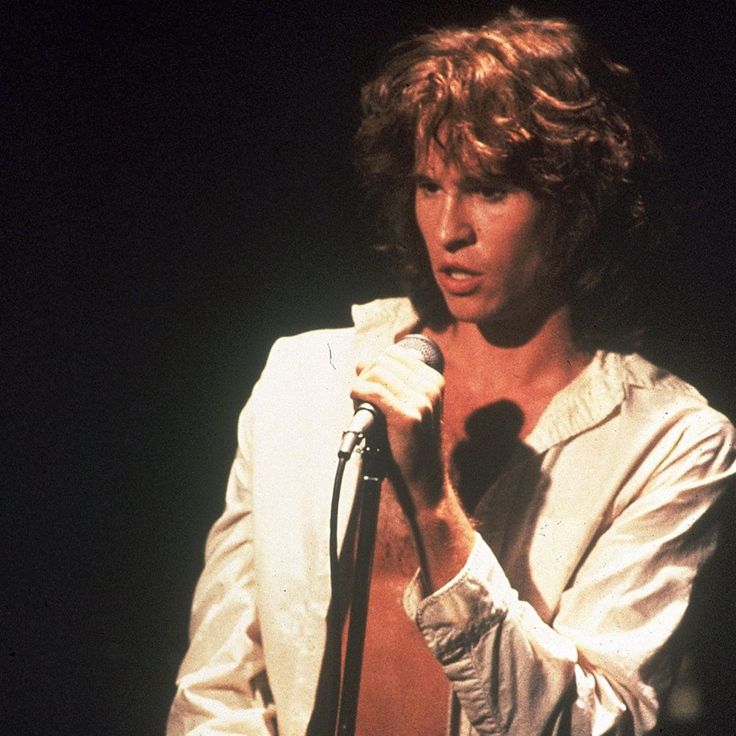 a man holding a microphone in his right hand and wearing a white suit on stage