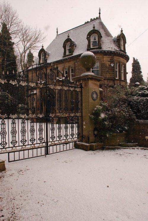 a large building with a gate and snow on the ground in front of it, surrounded by trees