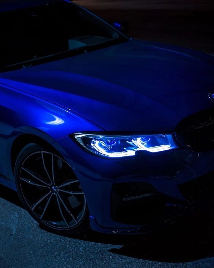 a blue bmw car parked on the side of the road at night with its lights on