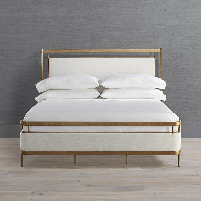 a bed with white linens and gold frame against a gray wall in a bedroom