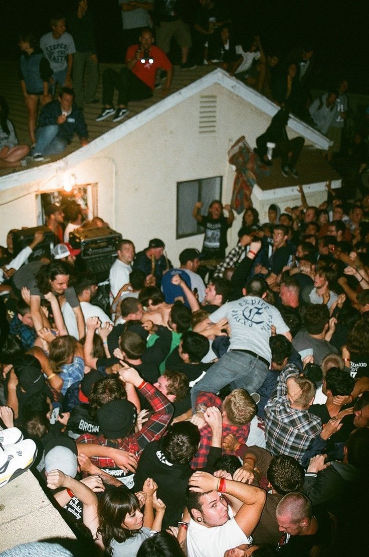 a large group of people are gathered around a house and one person is on the roof