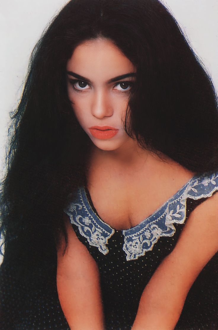 a woman with long black hair and blue eyes is posing for a photo in front of a white background