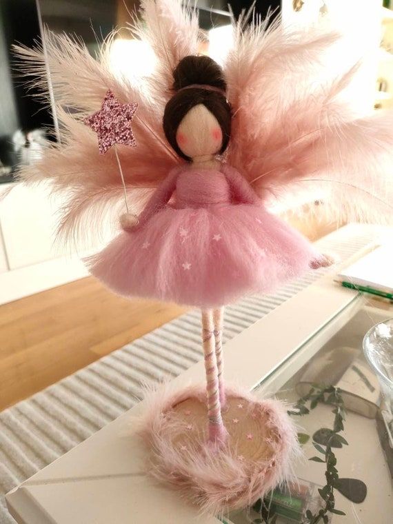 a doll is dressed in pink and has feathers on her head, as she stands on top of a table