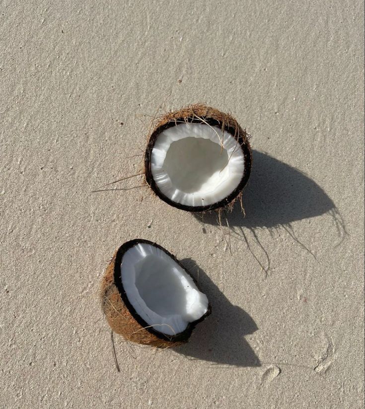 two coconuts are laying on the sand and one is cut in half to eat