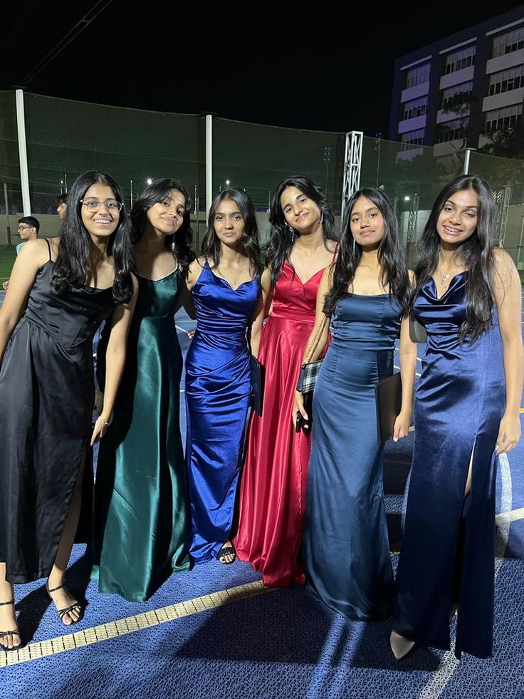 four women in long dresses posing for a photo at an event on a blue carpet