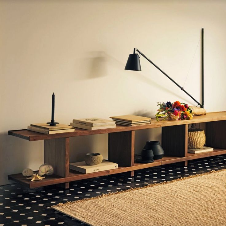 a shelf with books and vases on it in front of a wall mounted lamp