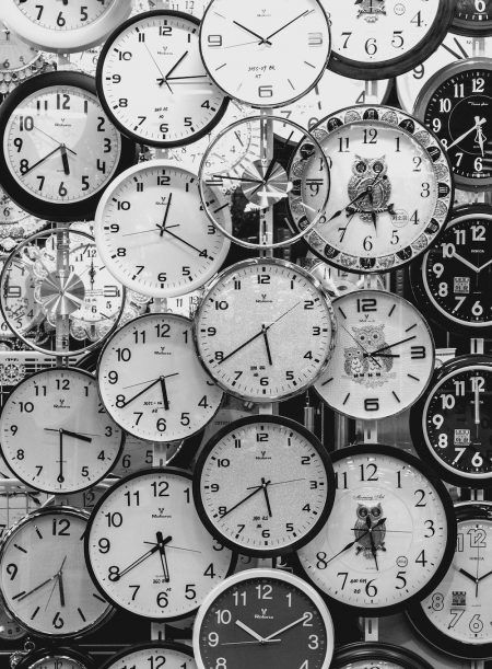 black and white photograph of many clocks with different time zones on them, all showing the same hour