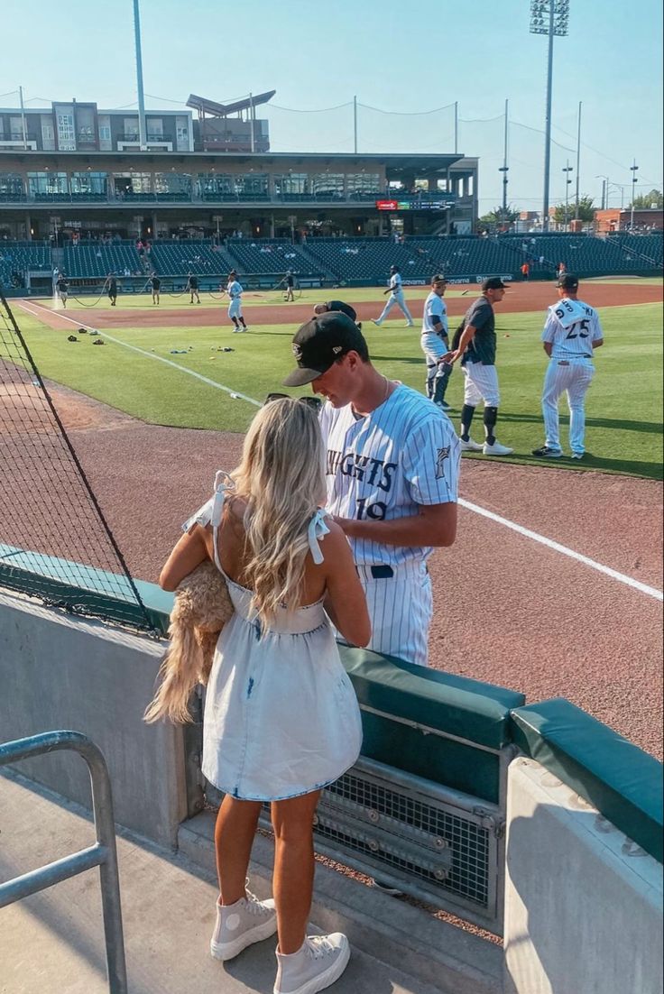 a man and woman standing next to each other at a baseball field with fans in the stands