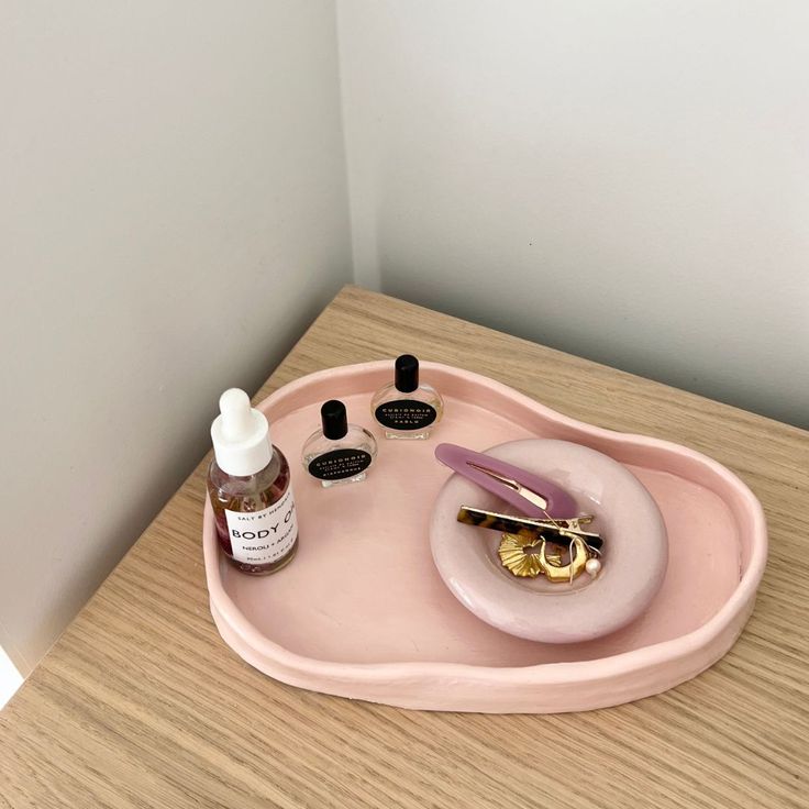 a pink tray with various items on top of it sitting on a wooden table next to a white wall