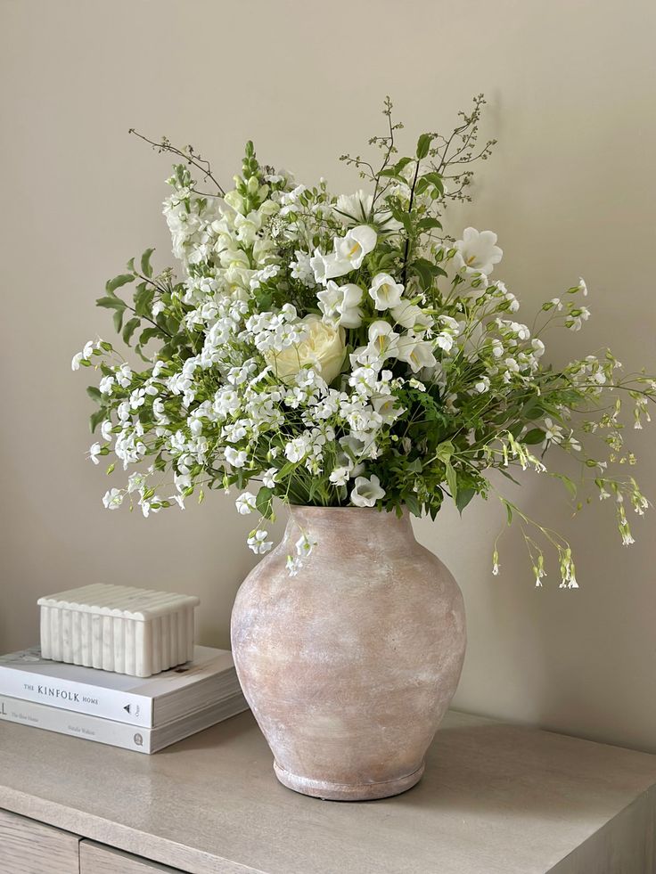 a vase filled with white flowers sitting on top of a table next to a book