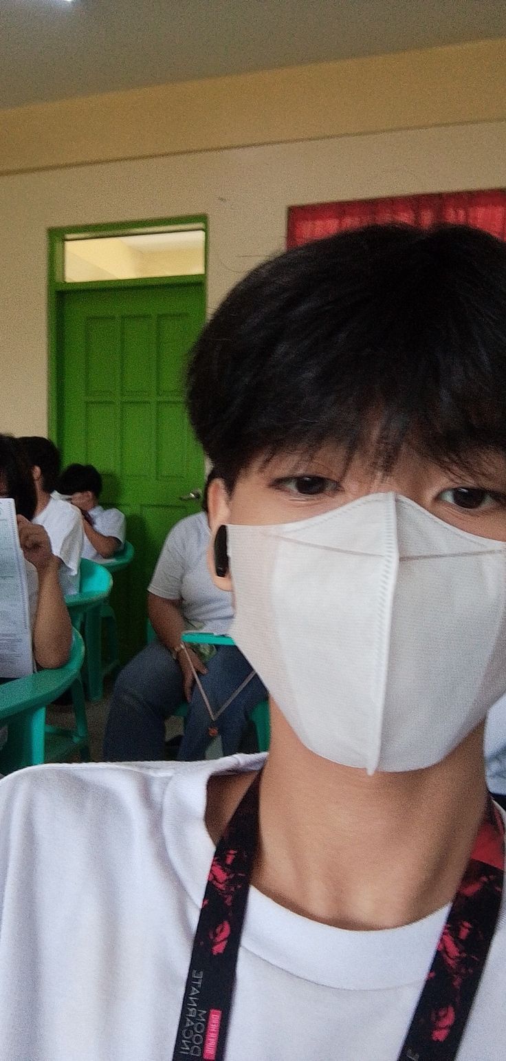 a young man wearing a face mask in a room full of people with green doors