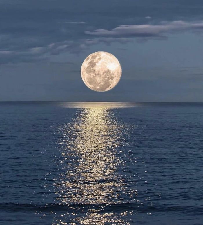 the full moon is reflected in the water at night, as it rises above the ocean