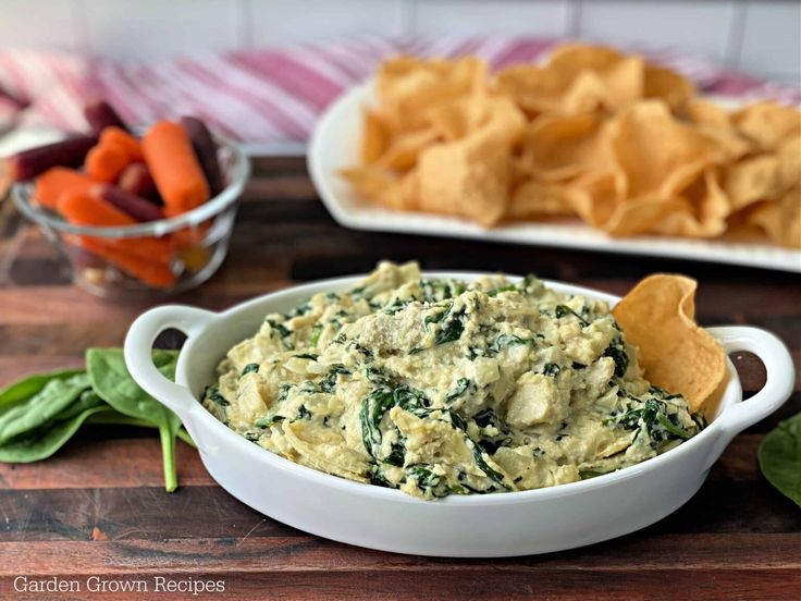 spinach dip with tortilla chips and carrots in the background