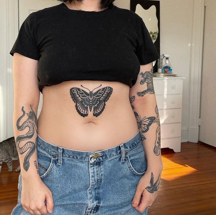 a woman with tattoos on her stomach is standing in front of a mirror and looking at the camera