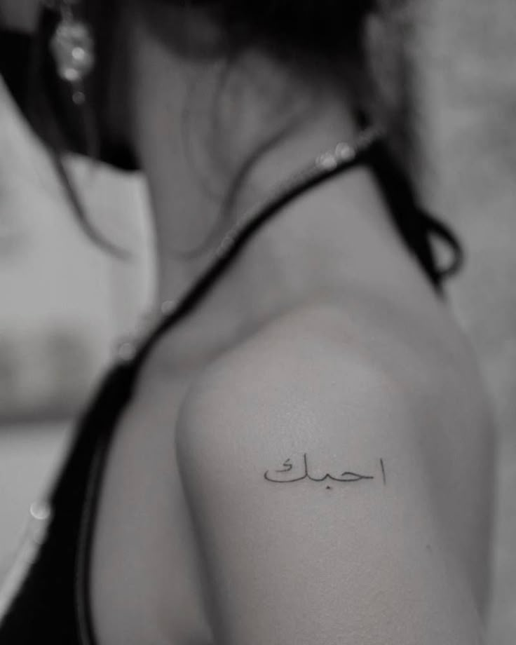 the back of a woman's shoulder with an arabic writing tattoo on her left arm