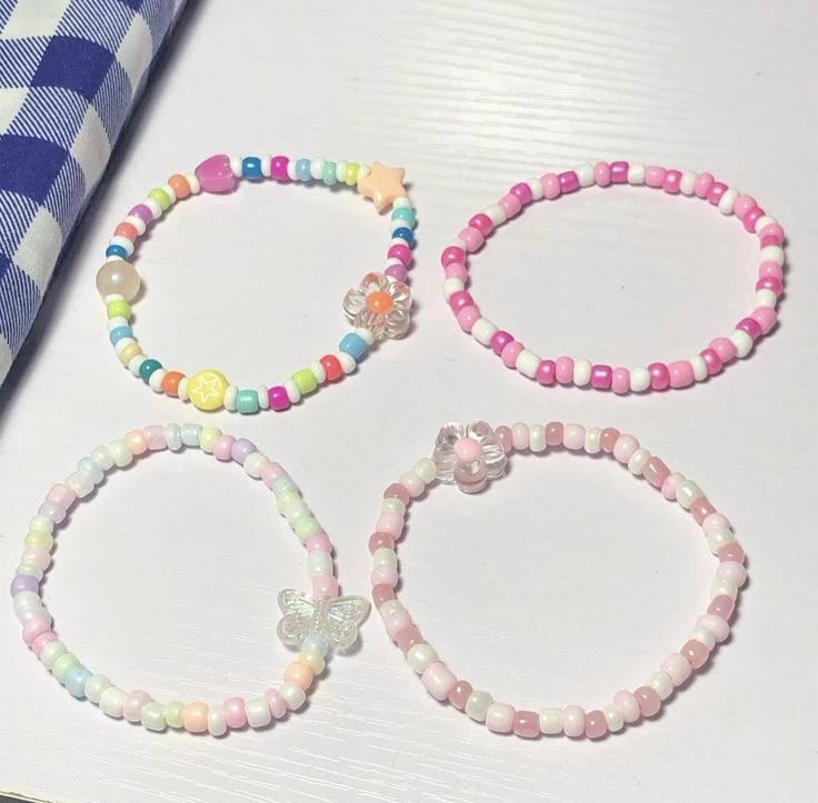 four bracelets with different colors and designs on them sitting next to a checkered table cloth