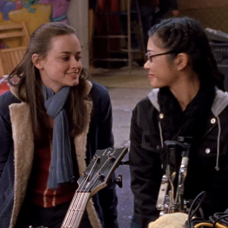 two young women sitting next to each other and one is holding a guitar in her hand