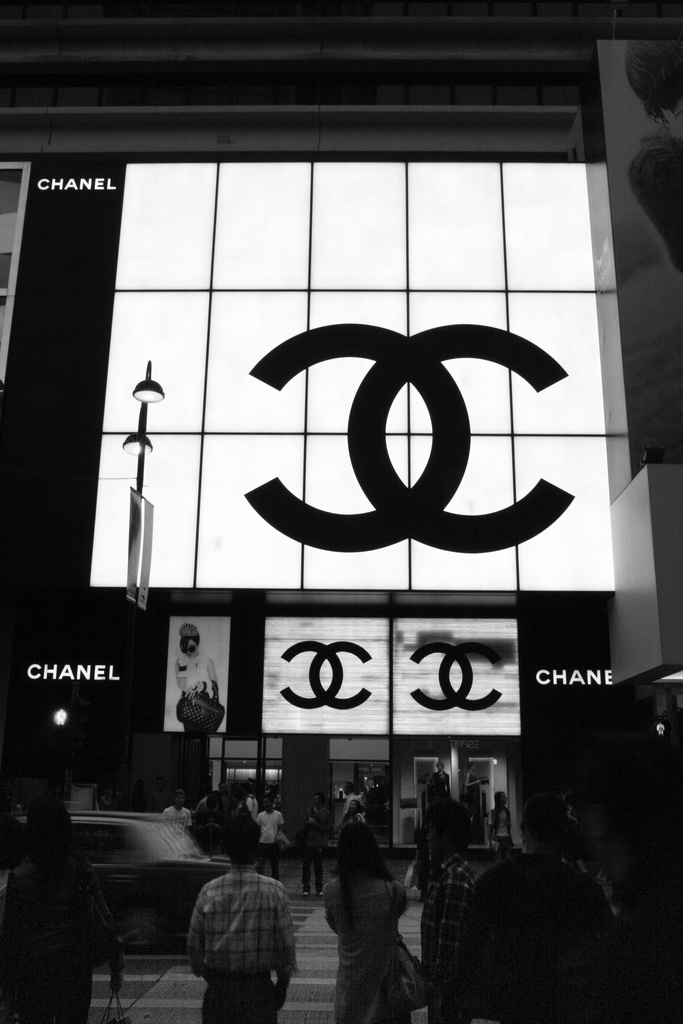 people walking in front of a chanel store with the logo projected on it's wall