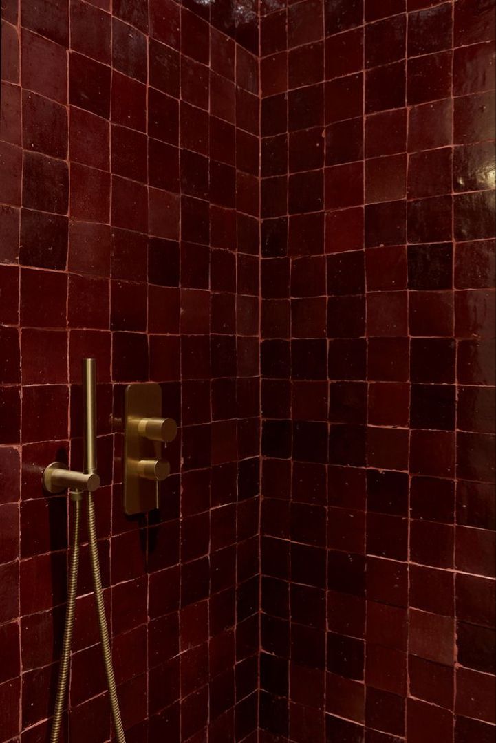 a red tiled shower with gold faucet and hand held shower head