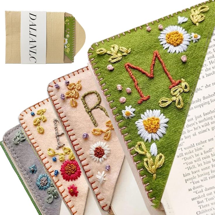 three bookmarks with embroidered letters and daisies on them, one has an open book