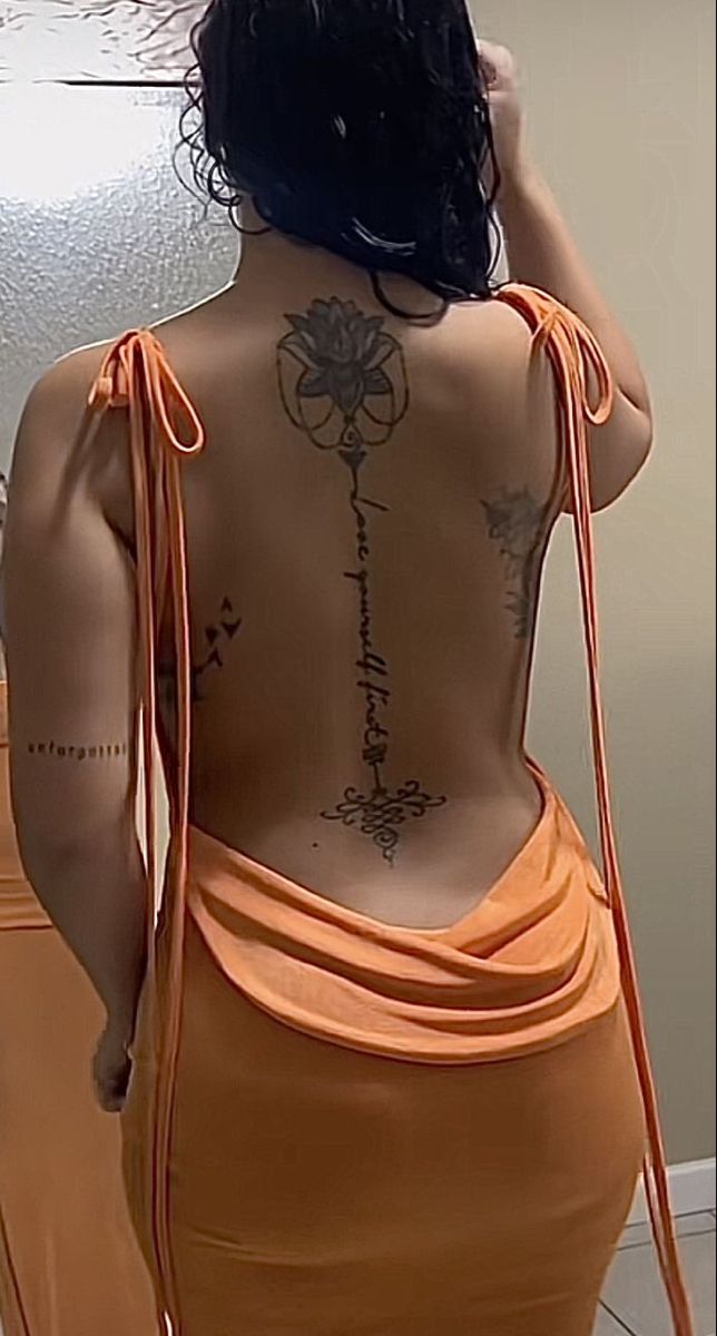 a woman in an orange dress looking at herself in the mirror with her back turned