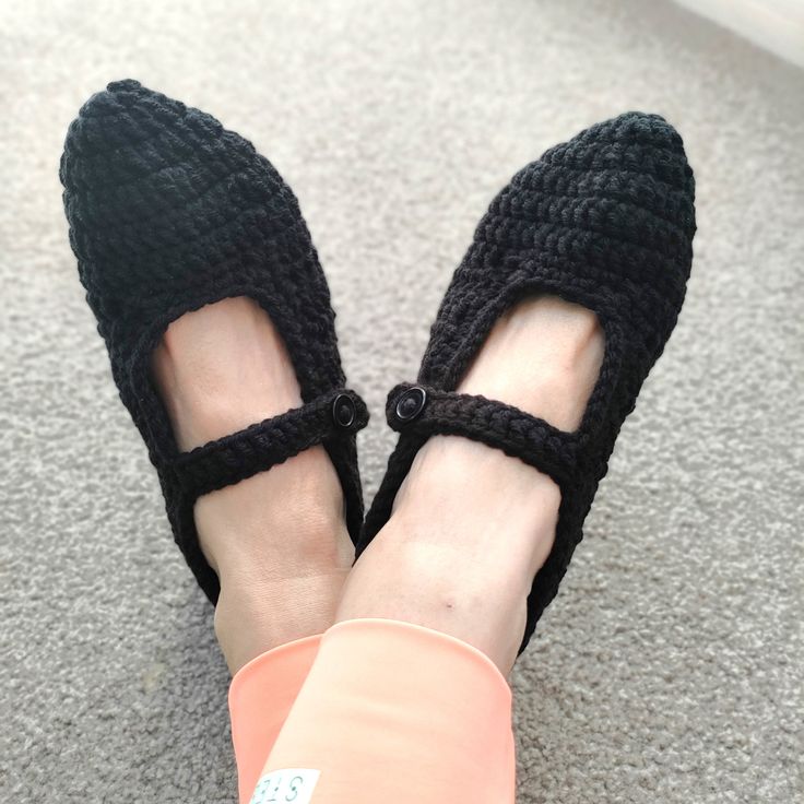 a woman's feet wearing black crocheted slippers on top of carpet