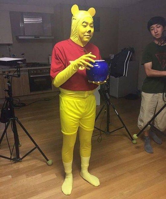 a man dressed as winnie the pooh holding a blue ball in front of him