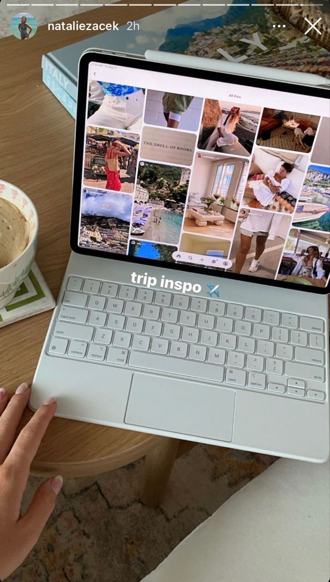 a person holding an open laptop computer next to a cup of coffee on a table