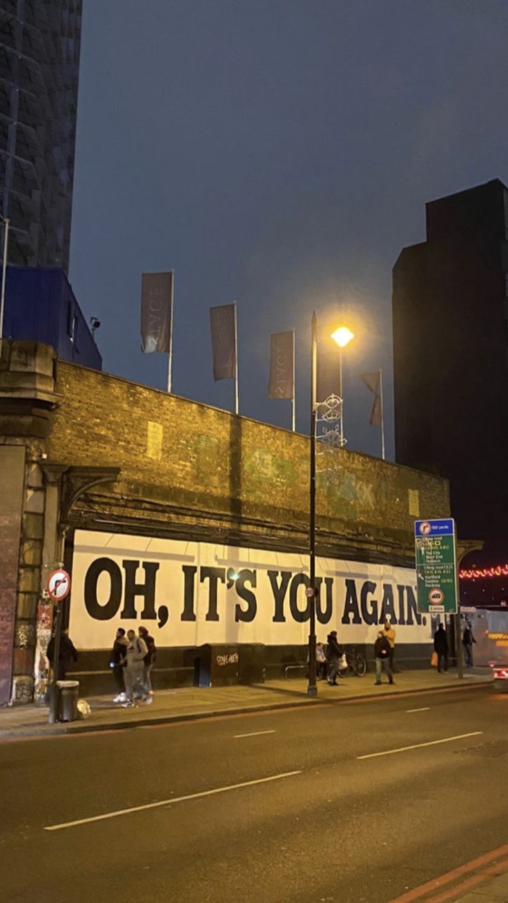 people walking down the street in front of a building with an advertisement on it's side