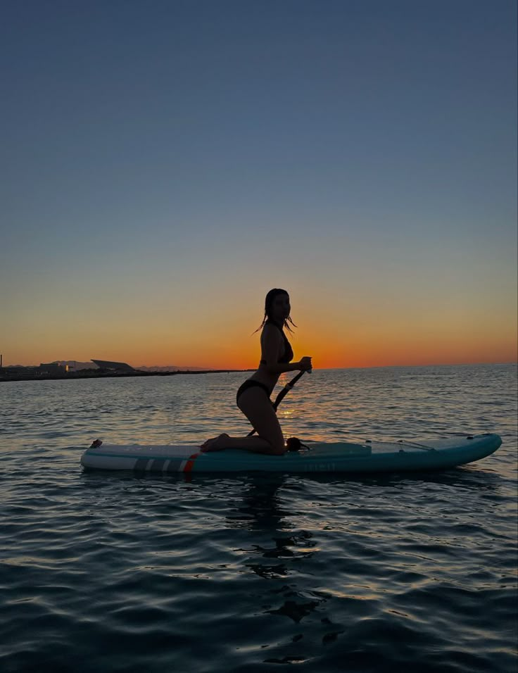 a woman riding on top of a surfboard in the ocean at sunset or dawn