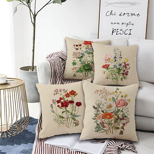 four pillows with flowers on them sitting next to a white couch in a living room