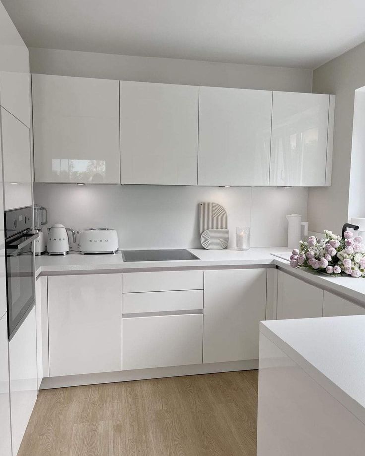 a kitchen with white cabinets and wood floors is pictured in this image, there are flowers on the counter