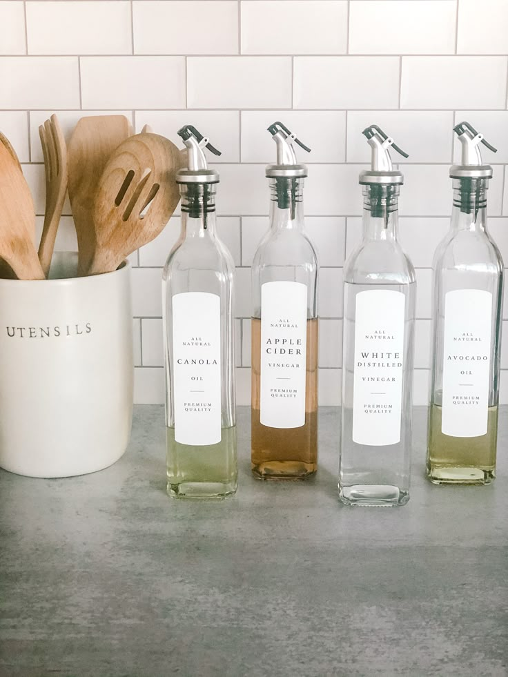 four bottles of liquid sitting on top of a counter next to wooden utensils