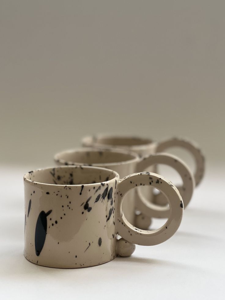 four coffee mugs sitting side by side on a white surface with black splatters