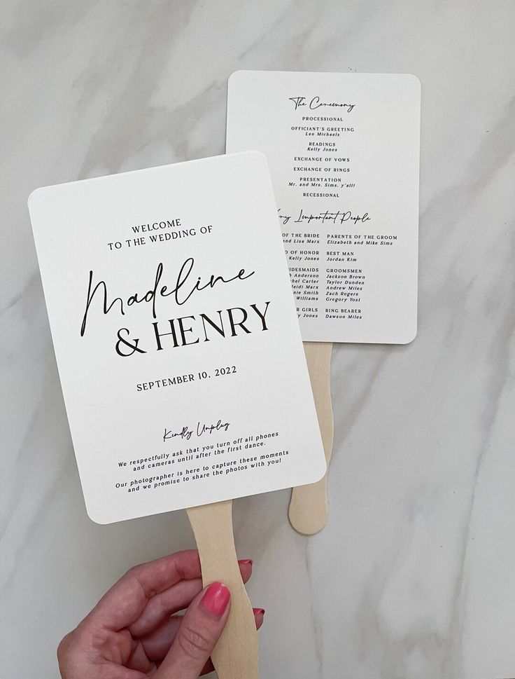 two fan shaped wedding programs are being held by someone's hand on a marble surface