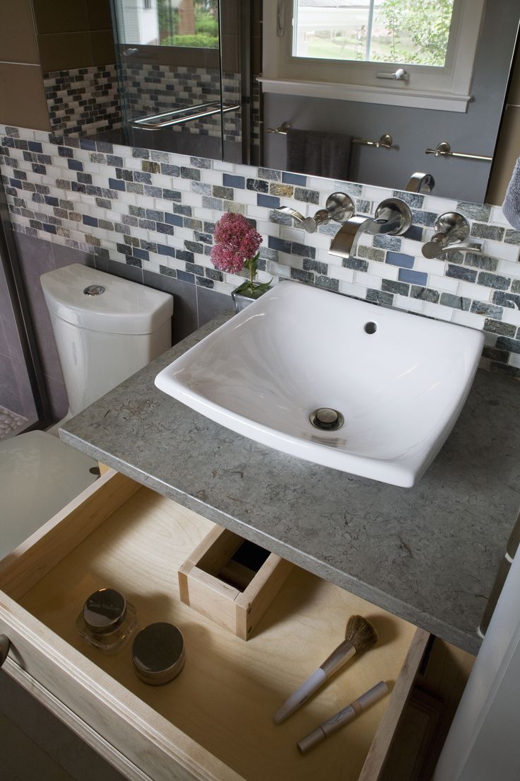 a white sink sitting under a bathroom mirror next to a wooden drawer with utensils in it