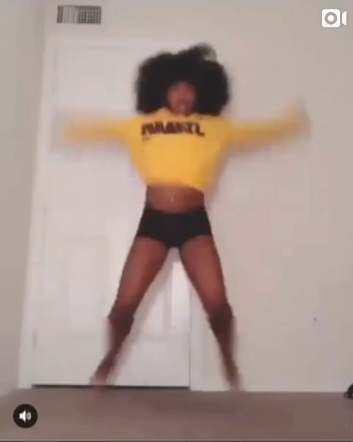 a woman in a yellow shirt and black shorts is dancing with her arms spread out