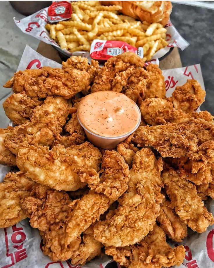 fried chicken with dipping sauce on top and french fries in trays next to it