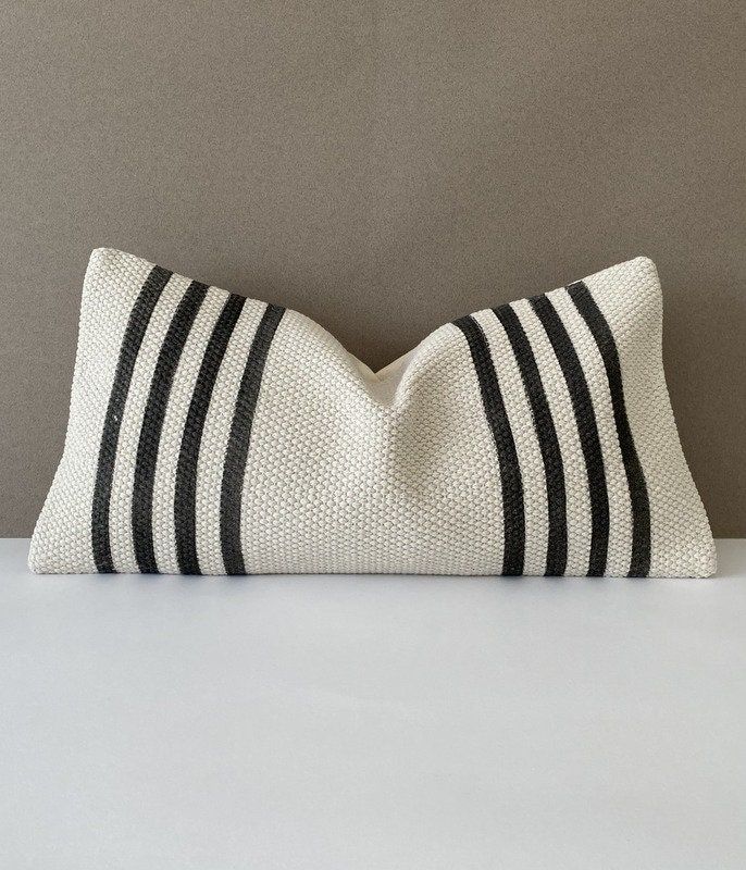 a black and white striped pillow sitting on top of a table next to a gray wall