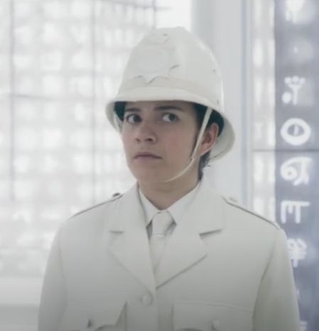 a woman wearing a white uniform and helmet in front of a window with words written on it