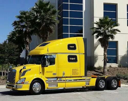 a bright yellow semi truck parked in front of a large white building with palm trees