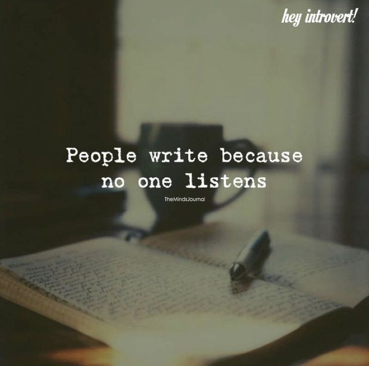 an open book sitting on top of a wooden table next to a cup and pen