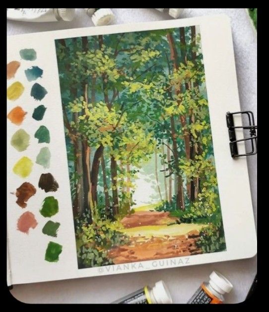 an artist's workbook with watercolors and paints on the table next to it