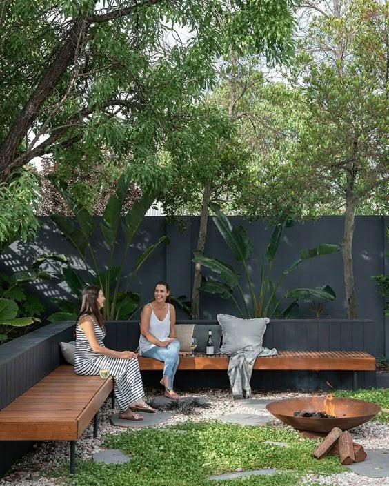 two women sitting on benches in the middle of a garden with fire pit and seating