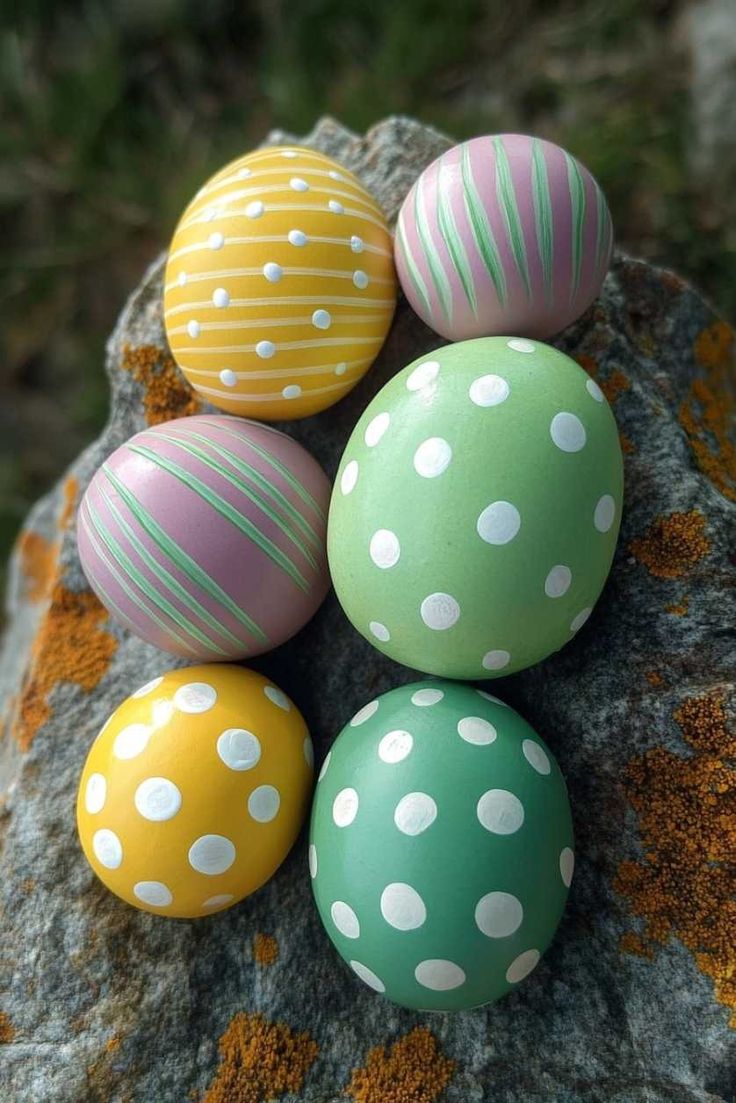 five painted easter eggs sitting on top of a rock with white dots and green stripes