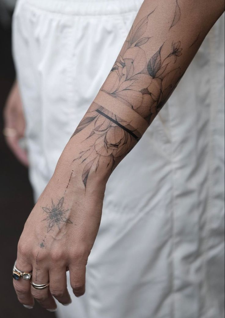 a person with a flower tattoo on their arm holding onto a white dress and gold ring