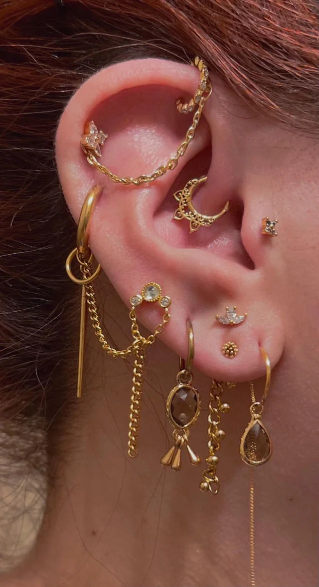 a woman wearing gold ear cuffs with dangling chains and earrings on her ears, all in different shapes and sizes