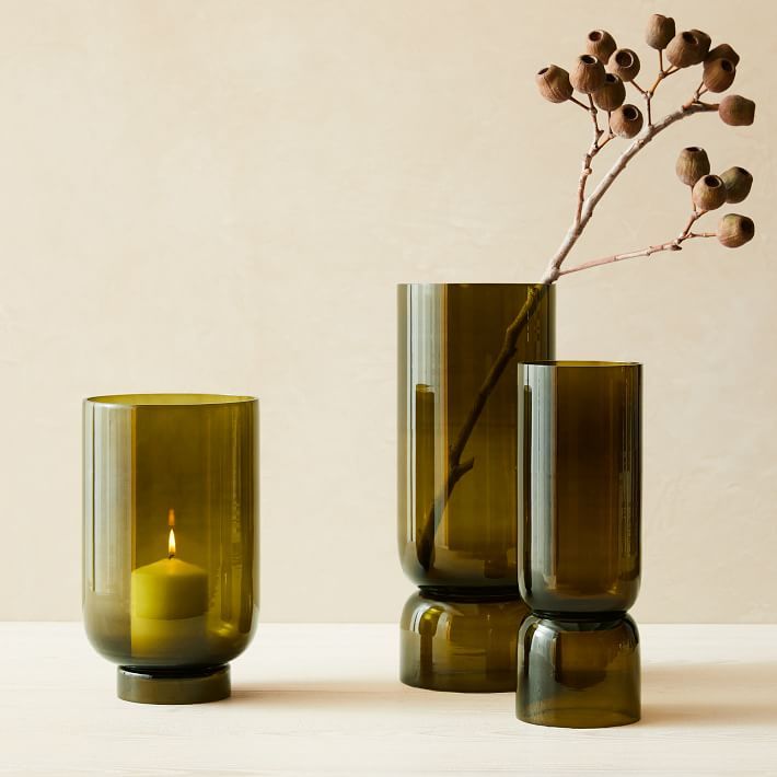 two green vases with a single candle in one and a small plant in the other