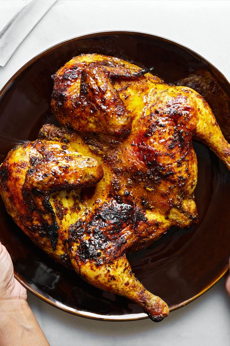 two hands holding a plate with cooked chicken on it and another person's hand next to the plate